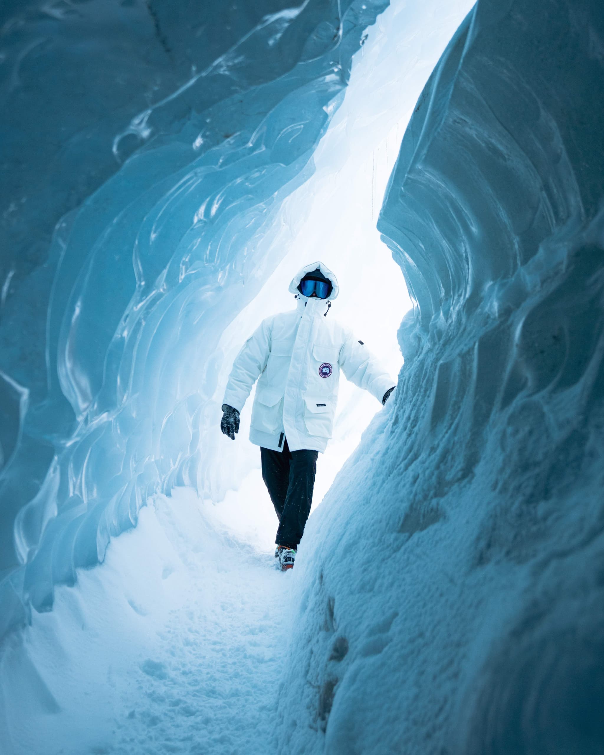 Person in a white jacket and black pants walking through a white tunnel of ice