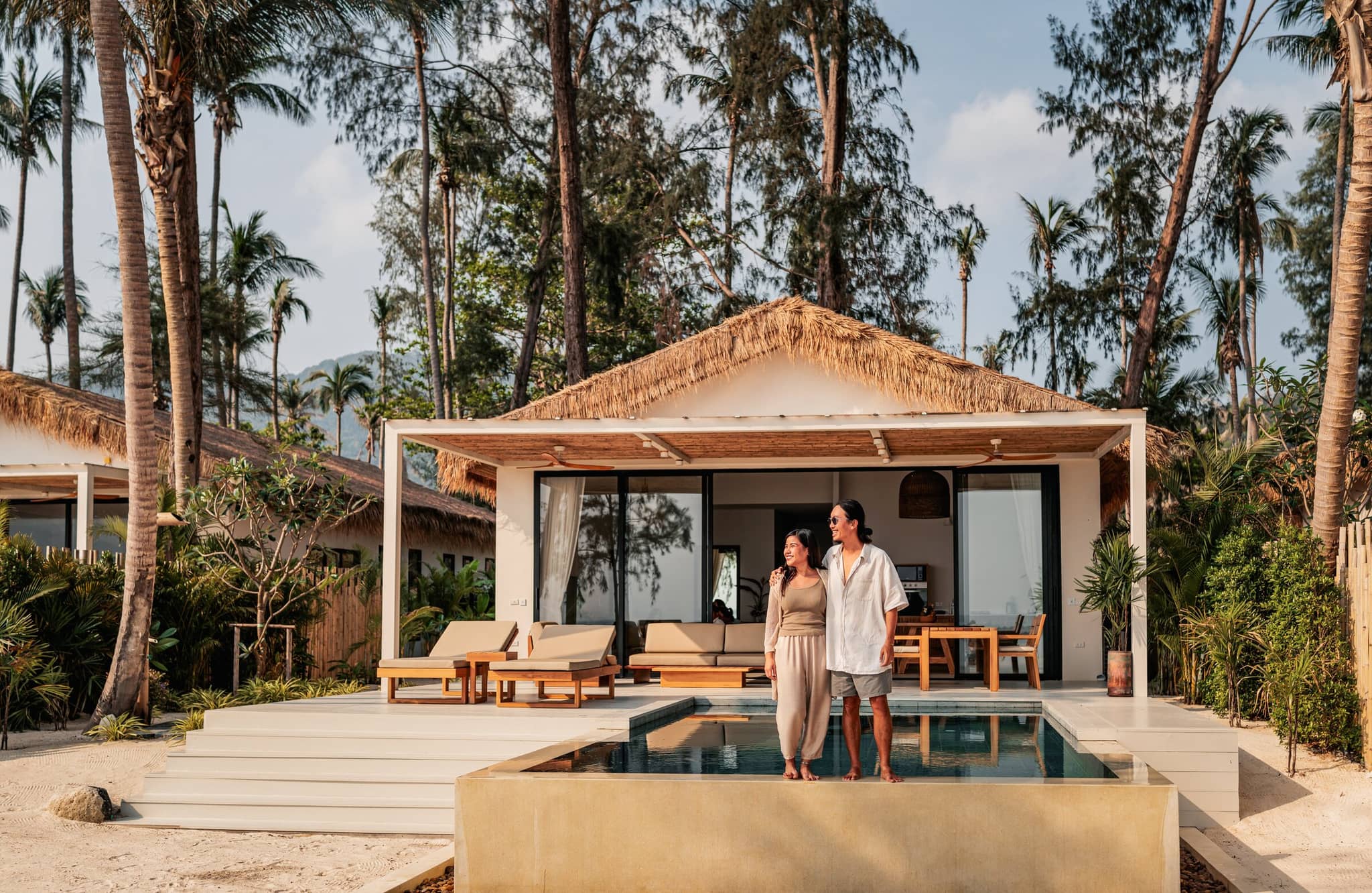 Couple enjoying a luxury travel experience at a beachfront villa surrounded by palm trees and private pool.