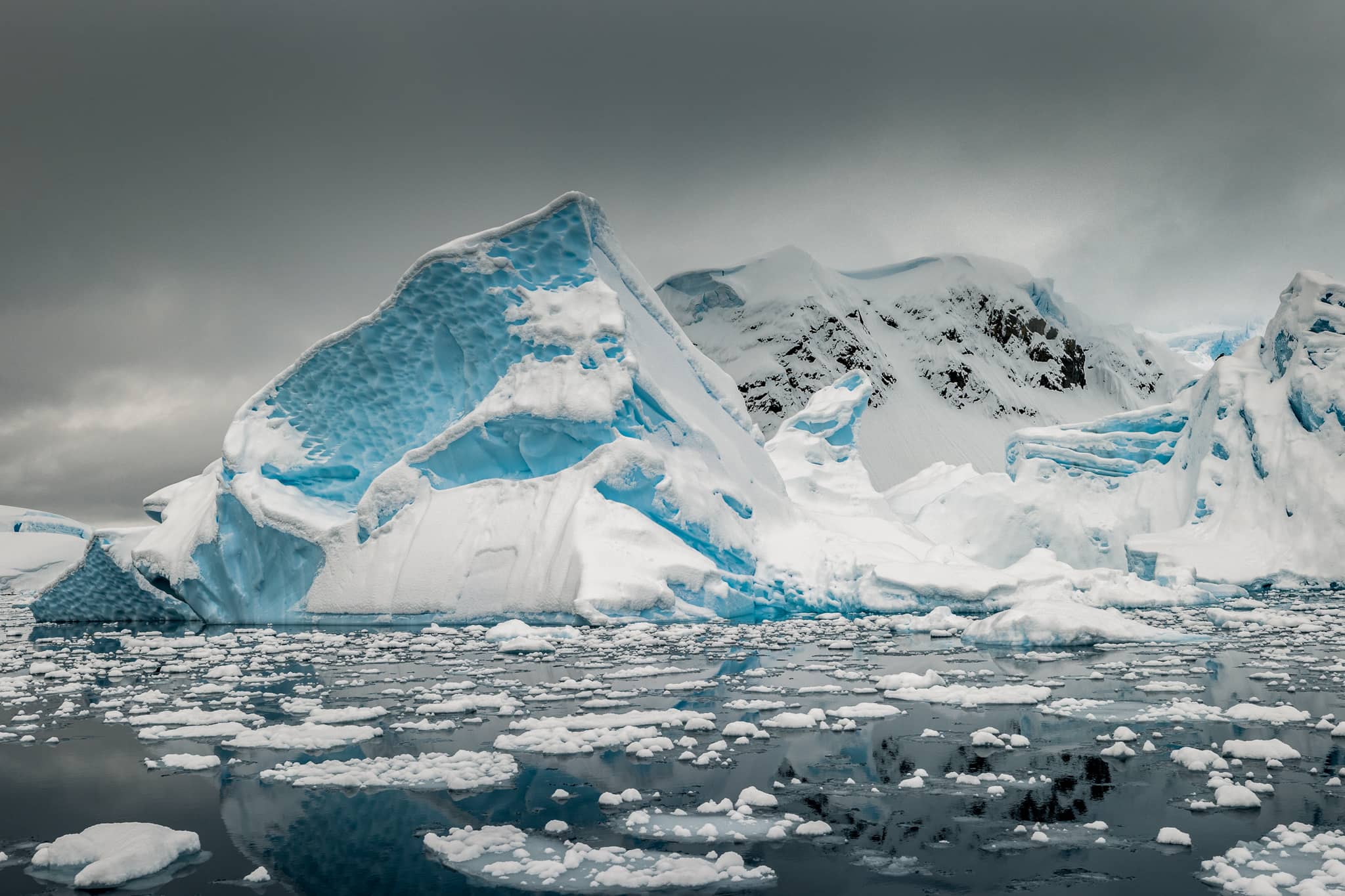Iceberg rising above a sea of nylas ice and small ice floes covered in fresh snow, Paradise Harbour, Antarctica