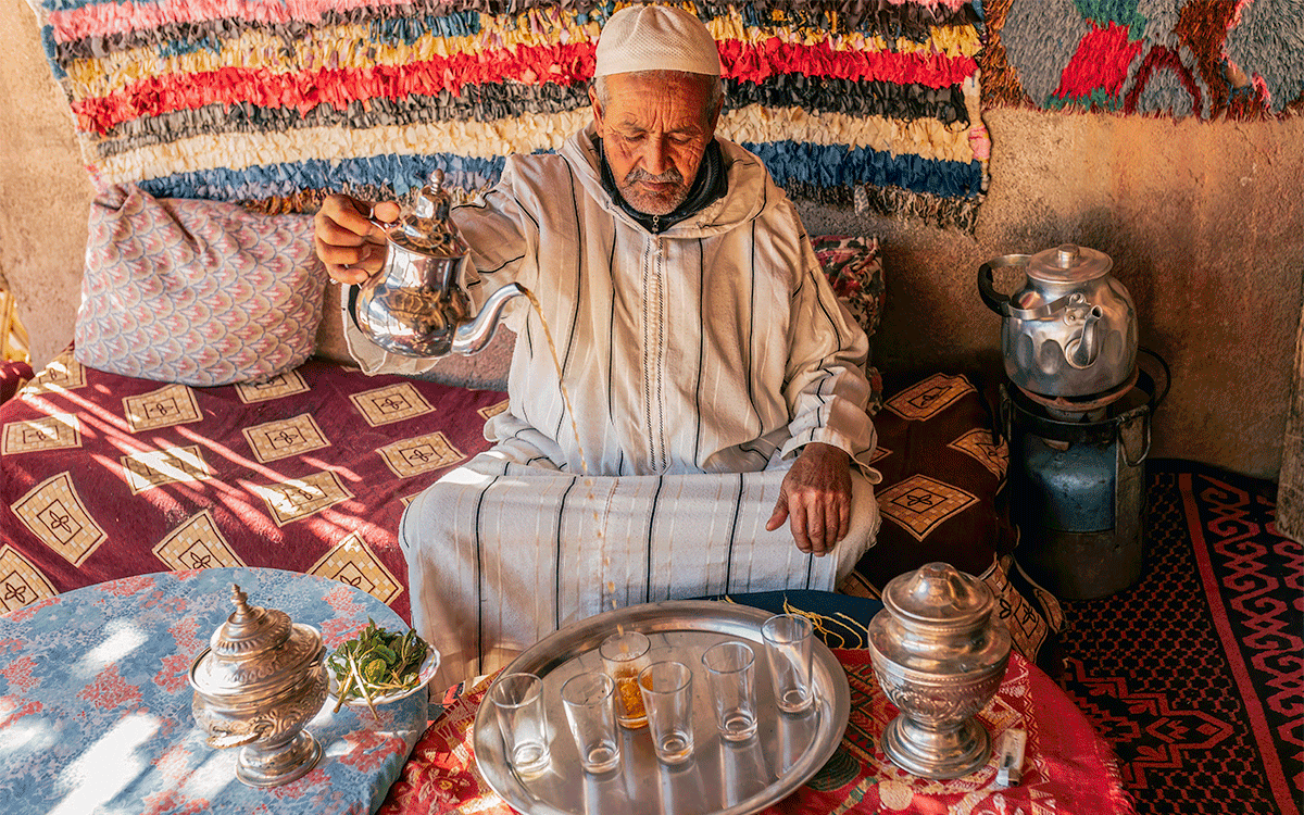 Moroccan man in traditional dress doing ritual preparation of mint tea on outdoor terrace